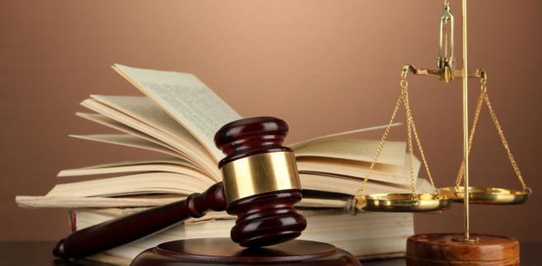 Na zdjęciu znajdyje się rozłożona książka, młotek sędziowski, waga Temidy. Wszystkie przedmioty leżą na&nbsp;biurku.